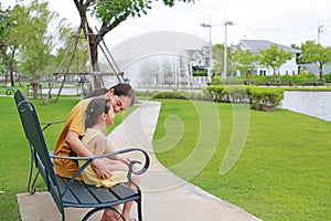 Asian mother and daughter relaxing sitting on bench in garden outdoors. Mum spending time together in summer park