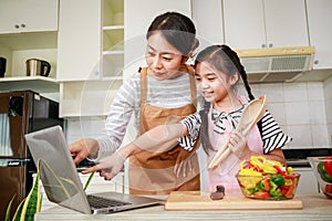 Asian mother and daughter see a menu in computer notebook and preparing salad. Leisure activity