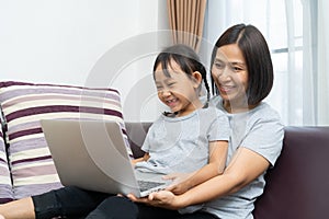 Asian mother and daughter using laptop studying homework online lesson at home