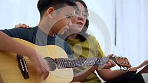 Asian mother embraces son, Asian boy playing guitar and mother embrace on the sofa and feel appreciated and encouraged. Concept of