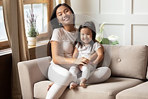 Asian mother embracing little daughter smiling looking at camera