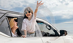 Asian mother father and children smiling sitting in compact white car looking out windows