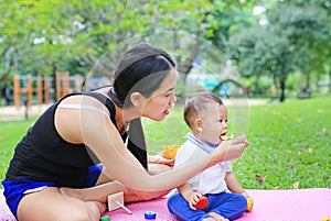 Asian mother feeding food for infant baby boy sitting on pink mattress mat in the garden