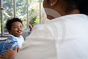 Asian mother feeding her 9 months old her cute little baby and African American helping for holding food plate At Home. Photo