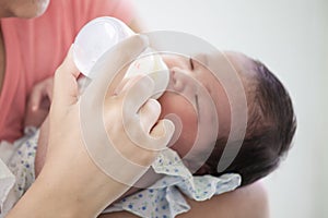 Asian mother feeding her newborn baby girl with milk bottle