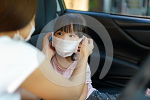 Asian mother help her daughter wearing protection mask to protect the coronavirus Covid-19 outbreak situation before in car go to