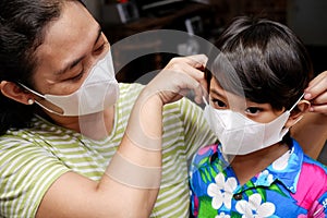 Asian mother helping cute little boy using healthy face mask