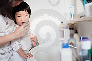Asian mother helping cute little toddler brushing her teeth, concept healthy happy child, health hygiene, kid oral hygiene, mother