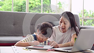 Asian mother is helping her daughter doing home work on coloring book in living room at home.