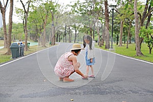 Asian mother helping her little daughter to put shoes on the road outdoor