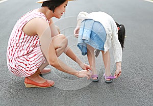 Asian mother helping her little daughter to put shoes on the road outdoor