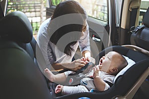 Asian Mother helping her little son to fasten belt on car seat in the transportation
