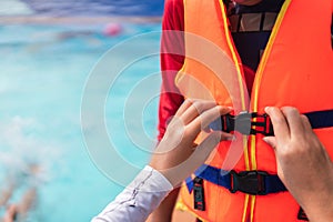 Asian mother helping her son to wear life jacket before playing in swimming pool, Selective focus