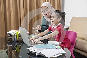 Asian mother helping little girl doing her homework with laptop at home