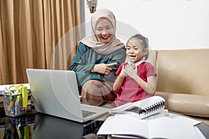 Asian mother helping little girl doing her homework with laptop at home