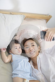 Asian Mother and her baby daughter are making selfie or video call to father in bed , Family , Home safety , parenthood ,