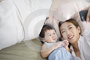 Asian Mother and her baby daughter are making selfie or video call to father in bed , Family , Home safety , parenthood ,