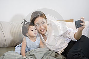 Asian Mother and her baby daughter are making selfie or video call to father in bed , Family , Home safety , parenthood ,