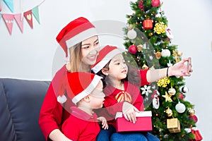 Asian mother with her children wearing christmas costume and taking photo themself by smartphone at home with christmas