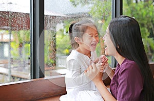Asian mother and her daughter playing with love near a window while raining day