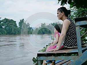 Asian mother and her little daughter by her side looking at murky muddy river after rainfall