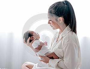 Asian mother hold or carry her newborn baby and look to baby face with love in bedroom