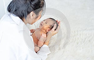 Asian mother hold her little newborn baby from bed and talk to each other and look happy