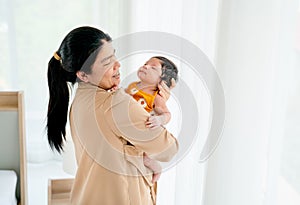 Asian mother hold sleeping newborn baby on her chest and stand in front of windows with white curtain with day light and she look