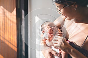 Asian mother holding her newborn baby at morning time, Baby smiles to mom, Birth and new life concept