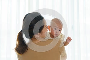 Asian mother is holding her newborn son in the bedroom at home, representing the love and bond between mother and son