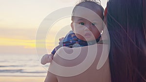 Asian mother holding her son at the sea sunrise beach front. Happy family vacation. Travel. Happy mom spending time with baby at