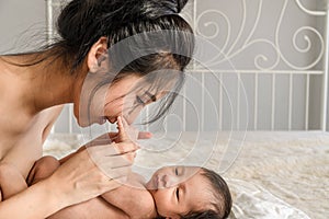 Asian mother holding and kissing her cute infant baby boy on bed