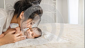 Asian mother holding and kissing her cute infant baby boy on bed