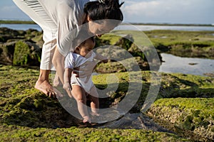 Asian mother holds the baby when the baby`s feet are touched to the sand beach