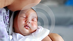 Asian mother holds close and kisses her newborn baby boy in her bedroom