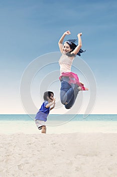 Asian mother jumping with daughter at beach