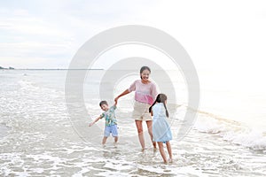 Asian mother and kids enjoy playing on tropical sand beach at sunrise. Happy family mom and child having fun in summer holiday