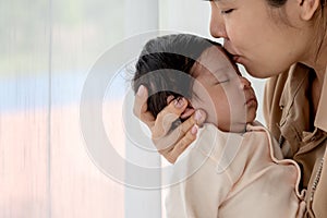 Asian mother kissing forehead his 1-month-old baby newborn daughter, with happy and love