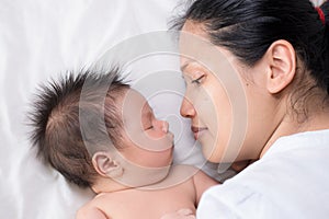 Asian mother lays on bed with newborn baby