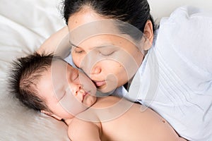 Asian mother lays on bed with newborn baby