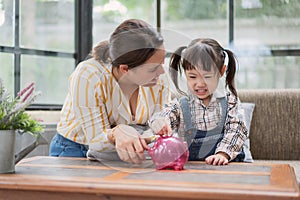 Asian mother and little daughter putting coins into piggy bank