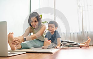 Asian mother and little son exercising in a online class with laptop