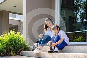 Asian mother looking her daughter primary students in uniform to wearing their own shoes infront of home in the morning school photo