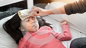 Asian mother measuring temperature girl with digital thermometer in her mouth on bed at morning time, Sick child have cool towel