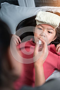Asian mother measuring temperature girl with digital thermometer in her mouth on bed at morning time, Sick child have cool towel