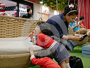 Asian mother paying her sole attention on a smartphone ignoring her two babies playing around