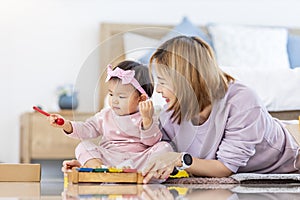 Asian mother is playing with her pretty smiling baby daughter with wooden toy block while spending quality time in the bed for