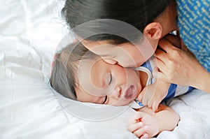 Asian Mother is playing and kissing her little baby boy on the bed