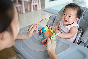 Asian mother playing toy with her baby sitting on the dinning chair at home. They are enjoy playing together with happiness.