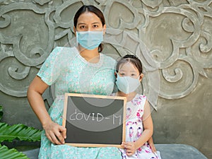 Asian mother is pregnant for five months and daughter wearing medical face mask and sitting hold the blackboard